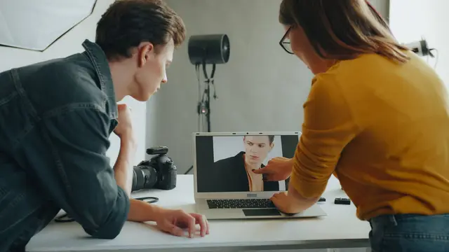 Two photographers review a portrait on a laptop during a studio session.